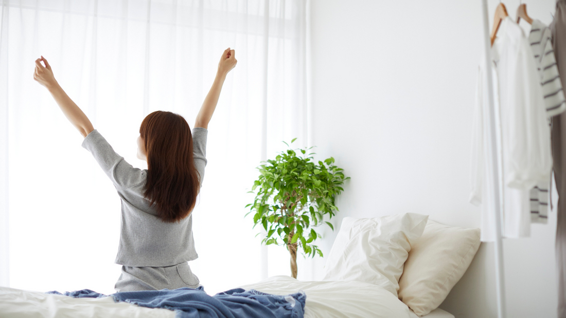 Woman stretching in bed with morning sunlight, supporting natural energy and low energy relief.